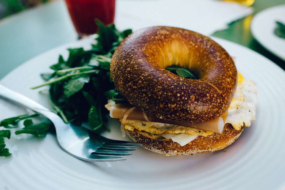 Bruch plate containing a ham and egg bagel sandwich and green salad